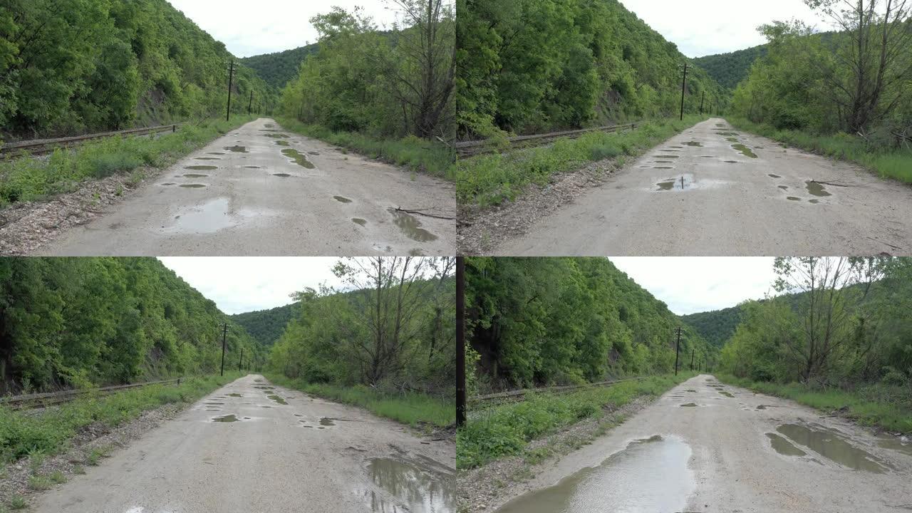 用水坑和附近的铁轨4k无人机镜头在泥泞的道路上向后飞行