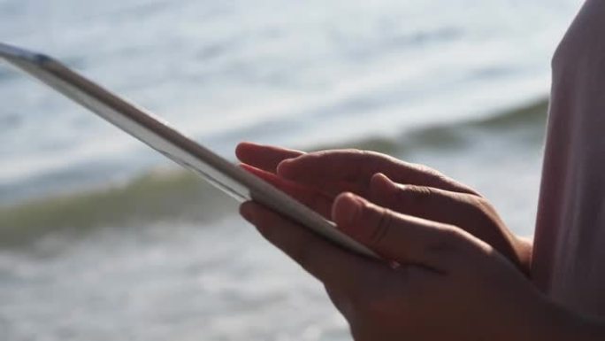 在度假期间，用数字平板电脑对抗海滩上的日出，生活方式概念。