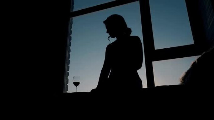日落时坐在房间酒杯附近的女孩的剪影