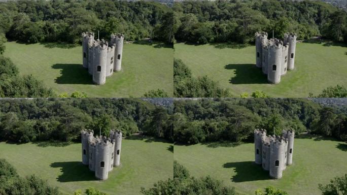 在阳光明媚的日子里，空中移动18世纪哥特式英国愚蠢城堡，三座炮塔，背景是绿色的林地