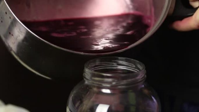一名男子将榨出的葡萄汁倒入玻璃罐中。在流行病期间制作自制葡萄酒。特写。