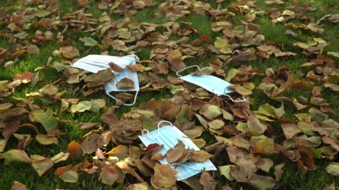 带秋叶的草地上的保护性蓝色一次性医用口罩