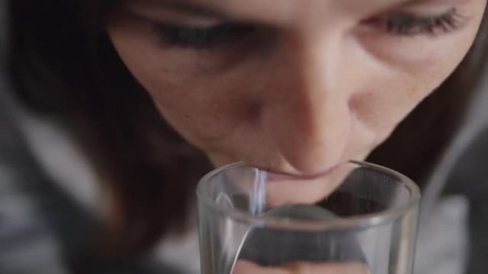 一名妇女服用维生素D3药丸和饮用水的特写