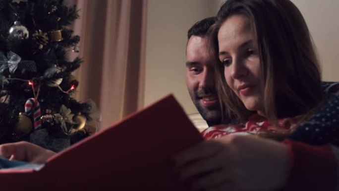 美丽的夫妇在圣诞节坐在沙发上看相册。