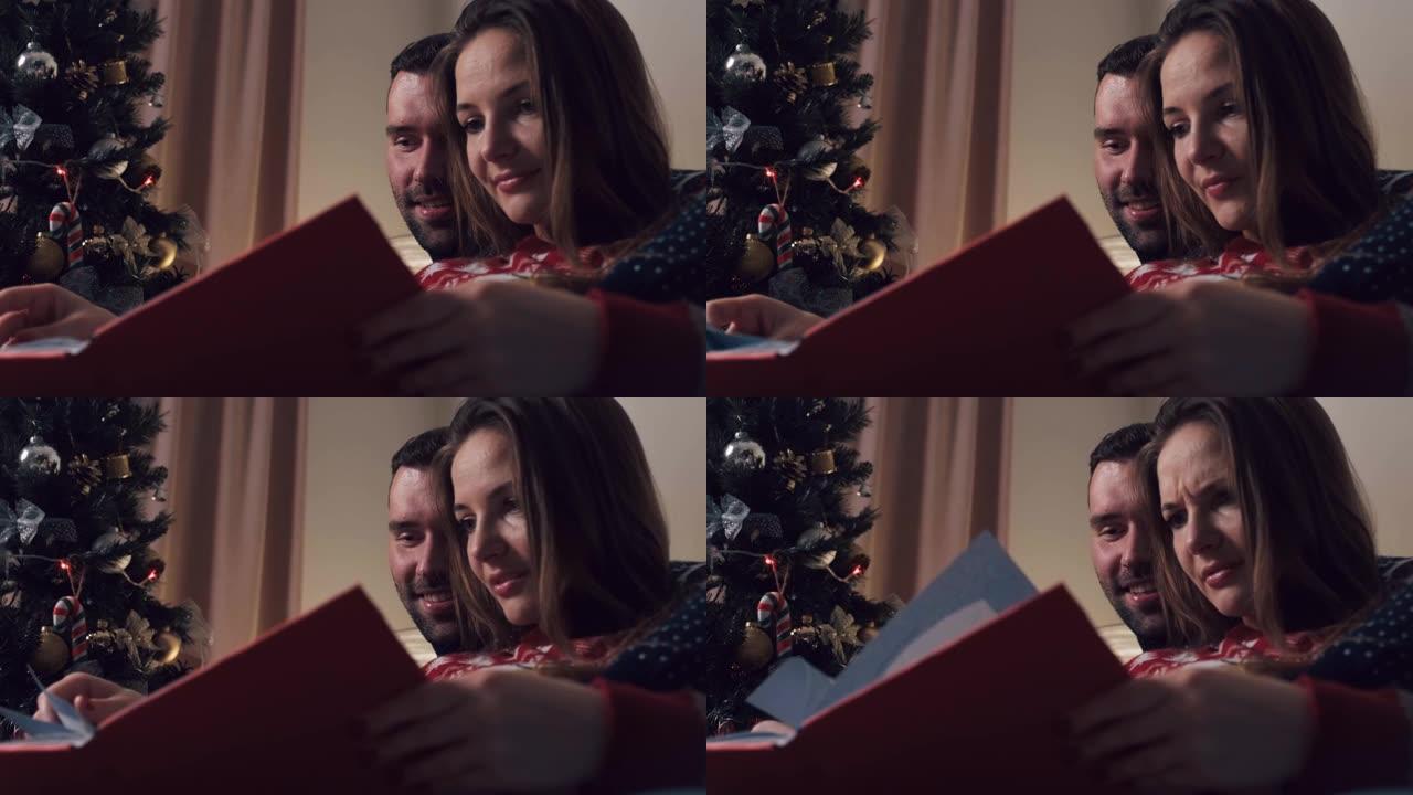 美丽的夫妇在圣诞节坐在沙发上看相册。