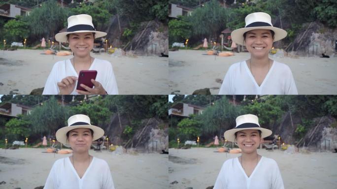 一位穿着白色连衣裙和白色帽子的年轻亚洲女性游客在海边的日子里微笑着享受假期