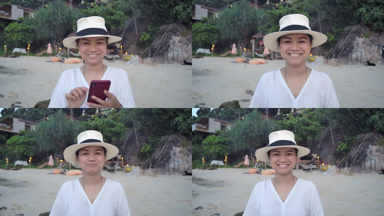 一位穿着白色连衣裙和白色帽子的年轻亚洲女性游客在海边的日子里微笑着享受假期