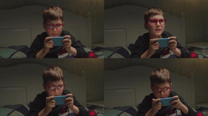 穿着睡衣和眼镜的青春期孩子在床上看手机应用程序。男孩在家玩手机游戏。