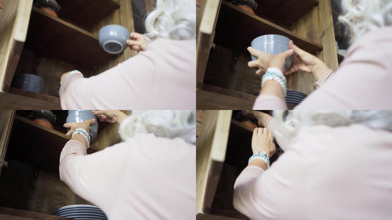 戴蓝色手镯的老年女士把碗盘放在橱柜里