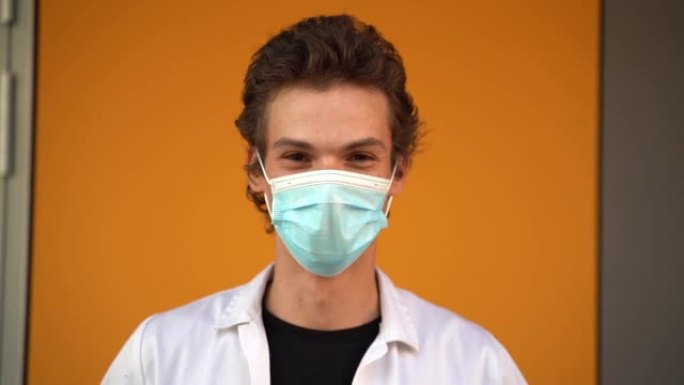 新型冠状病毒肺炎爆发期间，年轻男性医生戴着口罩靠在墙上的特写肖像。高质量4k镜头