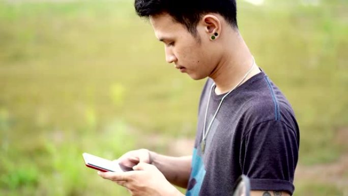 年轻的亚洲男子站着使用智能手机，对着镜头微笑