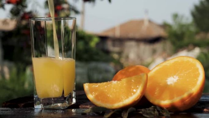 将橙汁倒入玻璃杯中。在乡间别墅和大自然的背景下，将橙汁倒入透明玻璃中，附近有新鲜切好的橙子。特写