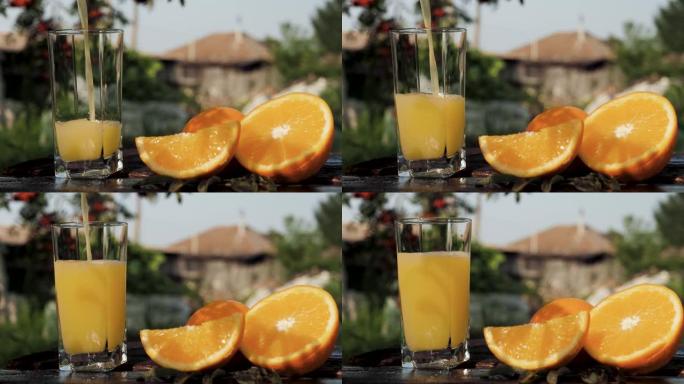 将橙汁倒入玻璃杯中。在乡间别墅和大自然的背景下，将橙汁倒入透明玻璃中，附近有新鲜切好的橙子。特写