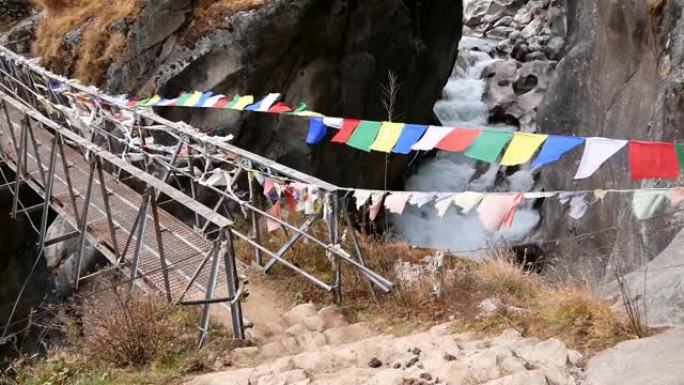 五颜六色的佛教祈祷旗附在金属桥上，在尼泊尔昆布地区夏尔巴人村庄Thame附近的远足小径上，狂风在野山