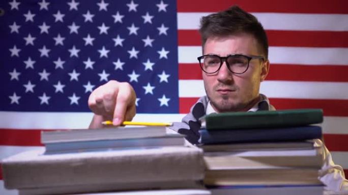 一个戴着眼镜的漂亮学生，穿着衬衫的书站在国旗前，困惑地在笔记本上写下想法