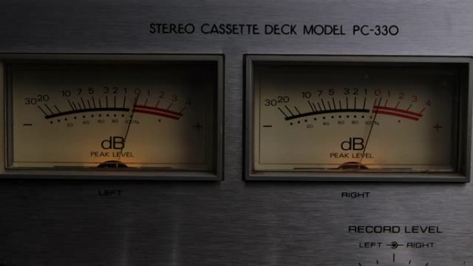 在老式电子声音音频设备上向上和向下的指示器dB分贝仪表针运动读数水平的极端特写。录音机上的仪表板。慢