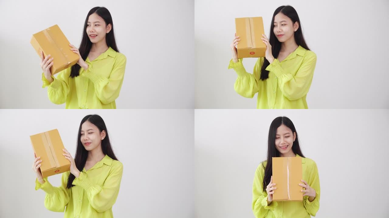年轻的亚洲女性微笑着拿着纸板箱在家里惊喜，快乐的女性带着包裹箱兴奋，礼物和礼物，包装送货，网上购物商
