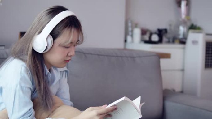 一个亚洲少女用耳机听音乐，在客厅背景中看书