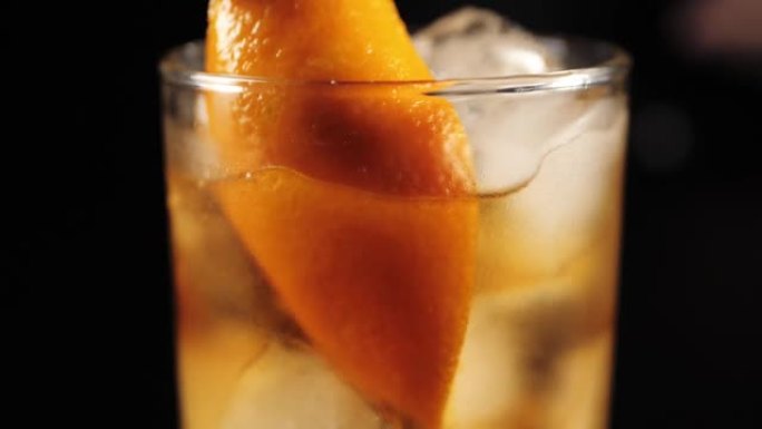 老式鸡尾酒。酒保将一片橘子皮放入鸡尾酒中。然后他把红樱桃放入成品饮料中。IBA官方鸡尾酒。特写