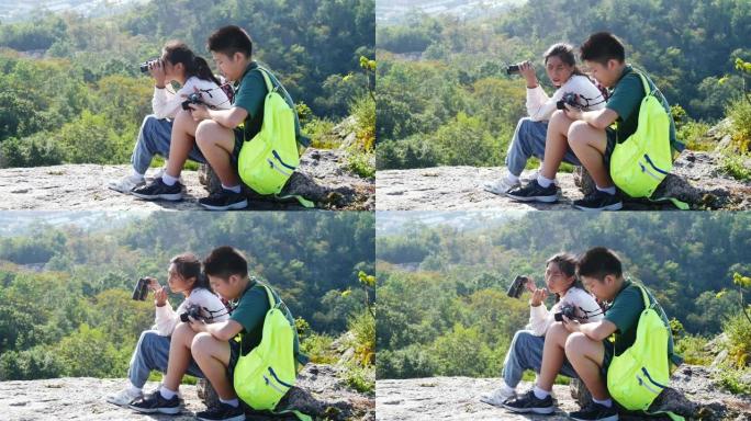 亚洲儿童在山顶上使用双筒望远镜和相机一起，冒险概念。