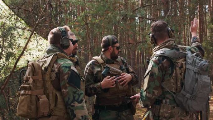 一群穿着制服和战术背心、蓄着胡须的中年士兵在一个临时森林基地讨论行动计划，并为行动做准备。指挥官使用