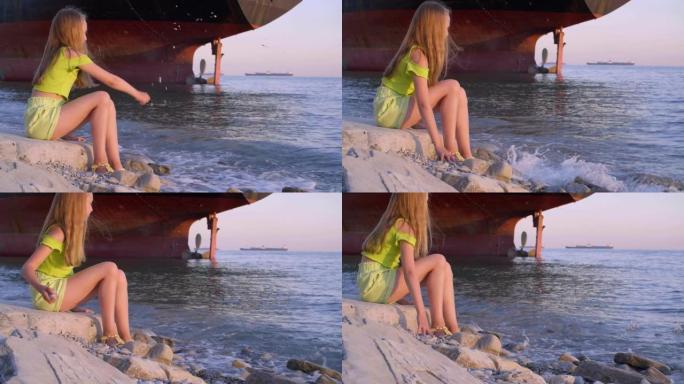 旅行少女少年向地平线上的货船景观上的海水投掷石块。旅游女孩在货船背景上向海边扔石头。