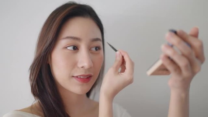美丽的亚洲女人在家美容她的脸，用棕色铅笔画眉毛，刷脸颊，给她的嘴唇上色。4k dci镜头。