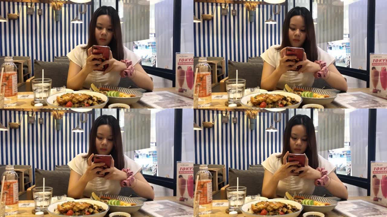 亚洲少女在餐厅吃饭时使用智能手机摄像头