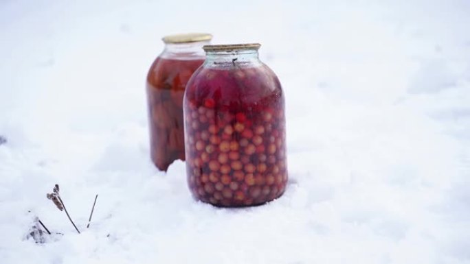 在街上的雪中关闭带有浆果和番茄罐头的罐装果汁。冬季在花园里密封的蜜饯和腌制蔬菜罐