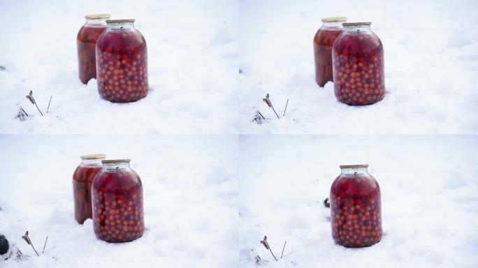 在街上的雪中关闭带有浆果和番茄罐头的罐装果汁。冬季在花园里密封的蜜饯和腌制蔬菜罐