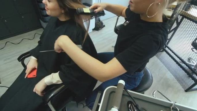 发型师发型师用梳子梳理女性客户的头发。美发美容院的女人。