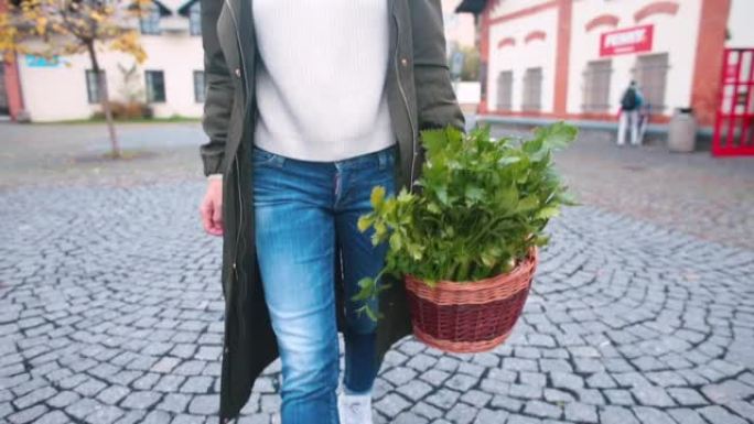 女人手里拿着篮子里的草药和蔬菜，沿着人行道走几步。