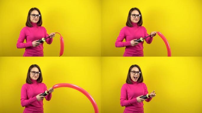 一名年轻女子用黄色背景上的泵给一个长长的红色气球充气。穿着粉色高领毛衣和眼镜的女孩。