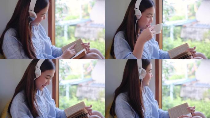 用耳机关闭可爱的女孩读一些书，坐在玻璃窗前，看起来她有快乐的情感