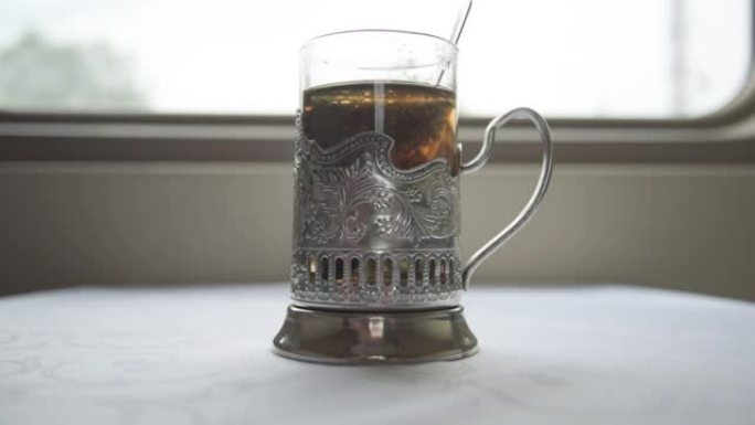 俄罗斯铁路。隔层的桌子上是传统杯架上的茶。一只手从杯子里拿出一个茶包的特写镜头。泡茶。旅程。