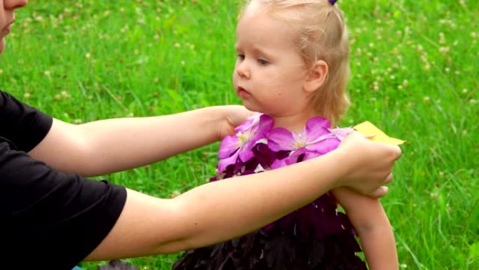 女人给可爱的小女孩穿上由花朵和叶子制成的紫色幻想连衣裙