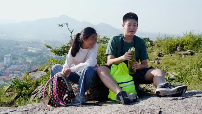 快乐的亚洲男孩和女孩在阳光明媚的户外冒险旅行中从自己的水食堂喝水。