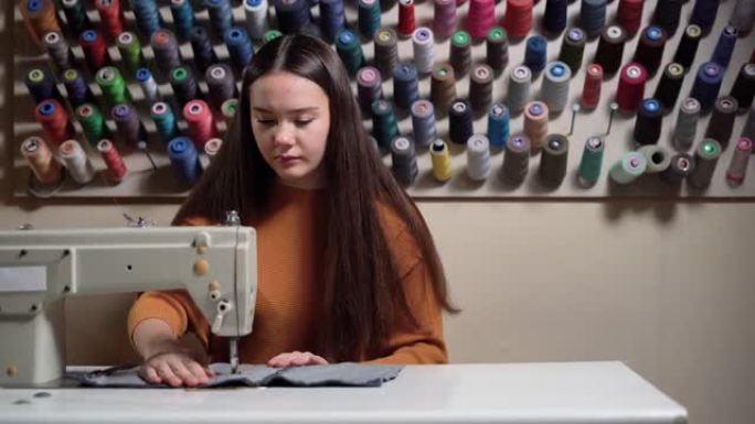 女孩在缝纫机上缝制牛仔裙，在家工作。一位年轻的设计师正在设置一台缝纫机。