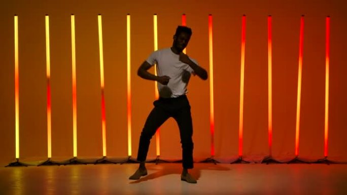 一名年轻黑人男子表演的萨尔萨舞。一名舞者在工作室中练习拉丁舞元素，背景是明亮的橘红色霓虹灯慢动作