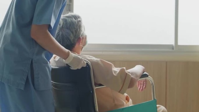 在医院照顾坐在轮椅上的成熟男性病人的亚洲护士。年轻妇女和老人戴上外科口罩，以预防covid - 19