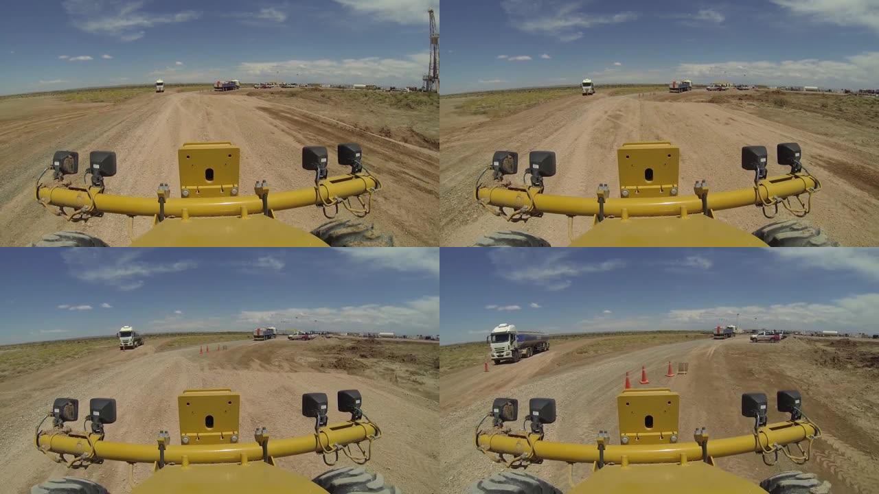 平地机在非常规油田内的土路上工作。(压裂)。