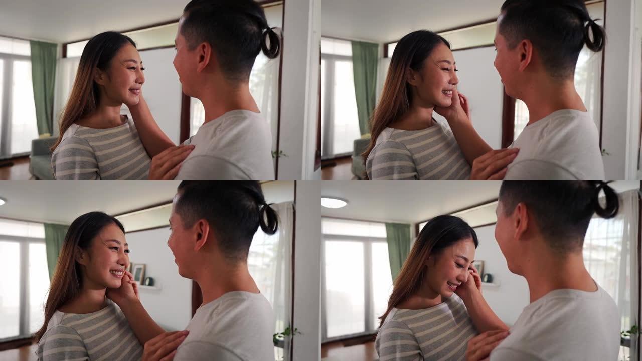 30多岁的亚洲年轻人在家里的客厅里抚摸着一个微笑的女人的脸颊。温柔浪漫的夫妻在舒适的房间里度过家庭时