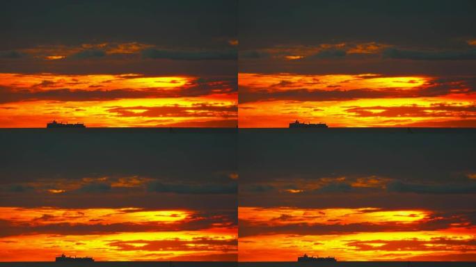 剪影货船在地平线海上缓慢移动和日落红黄橙天空