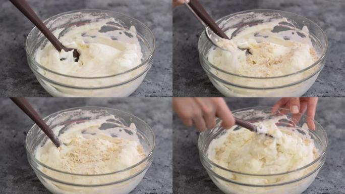 女人手中的硅胶刮刀小心地将切碎的腰果，糖和面粉的混合物放入搅打的蛋清中，在玻璃碗中烘烤基辅蛋糕