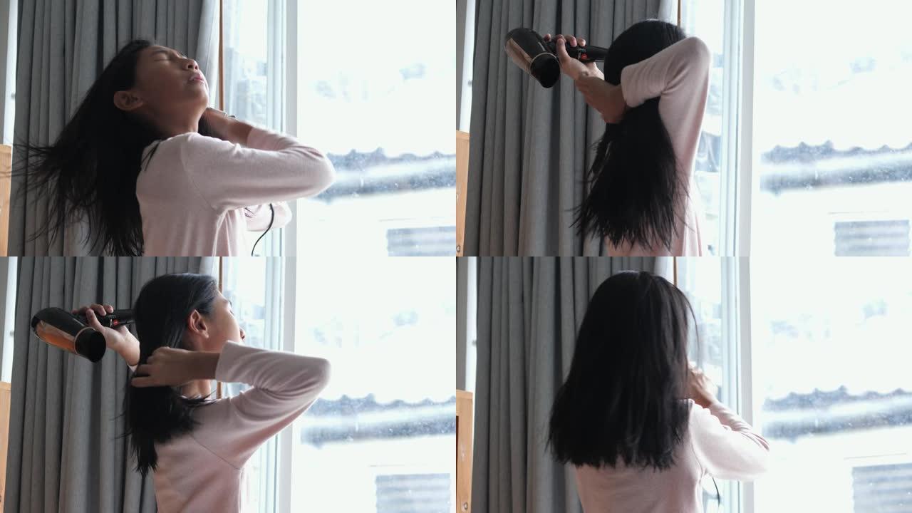 亚洲女孩在家里用吹风机为她潮湿的头发靠近窗户，生活方式的概念。