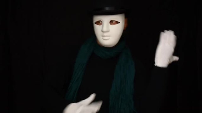 戴着白色面具的哑剧 -- 脸、帽子和白手套塑性跳舞，在黑色背景上表达感情。