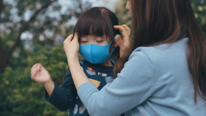 母亲在公园为小女儿戴上外科口罩，以防止感冒，流感和病毒的传播