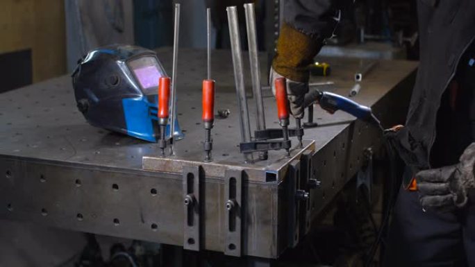 戴着防护面罩和手套的焊工使用焊接机在特殊的工作台上焊接金属零件。半自动气体保护焊。50 fps 4k