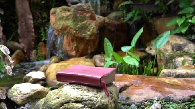 圣经坐落在带有迷你瀑布的岩石花园的石头上。