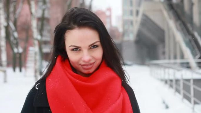 穿着黑色外套和红色围巾的年轻微笑女人在冬季城市摆姿势。
